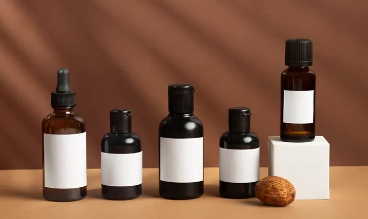 Five black bottles with blank labels and a small brown nut on a brown background.